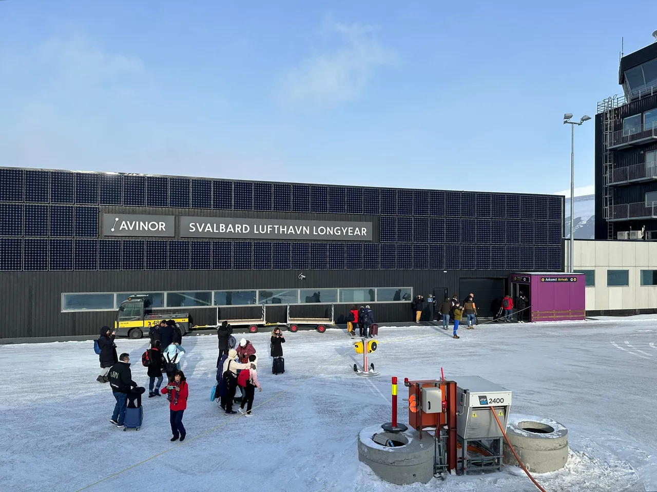 The dark terminal building of Svalbard Airport, Longyear, with the Avinor sign, and travellers with luggage on the snowy forecourt
