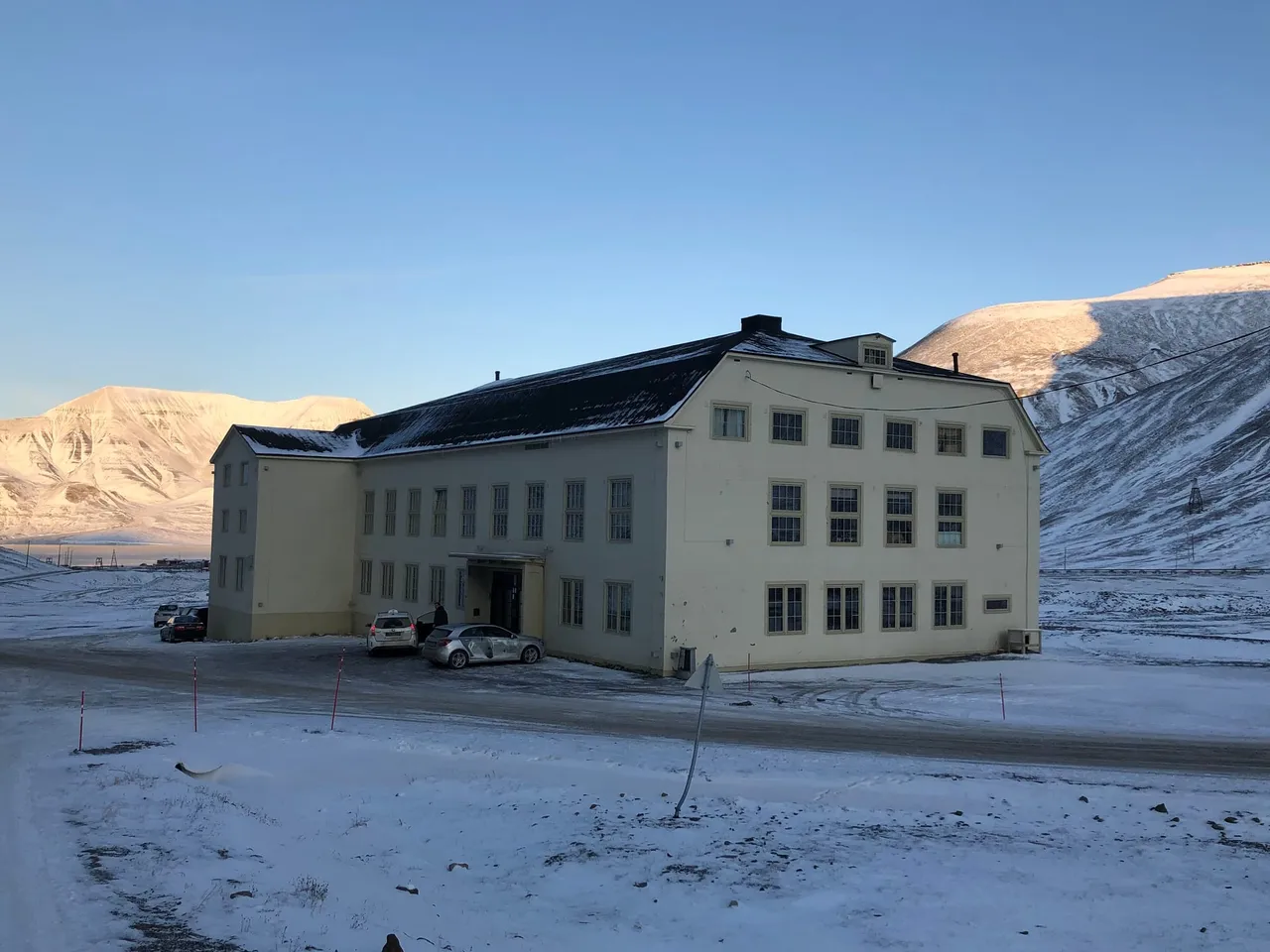 A large white two-storey building with a dark roof standing alone on a snowy slope