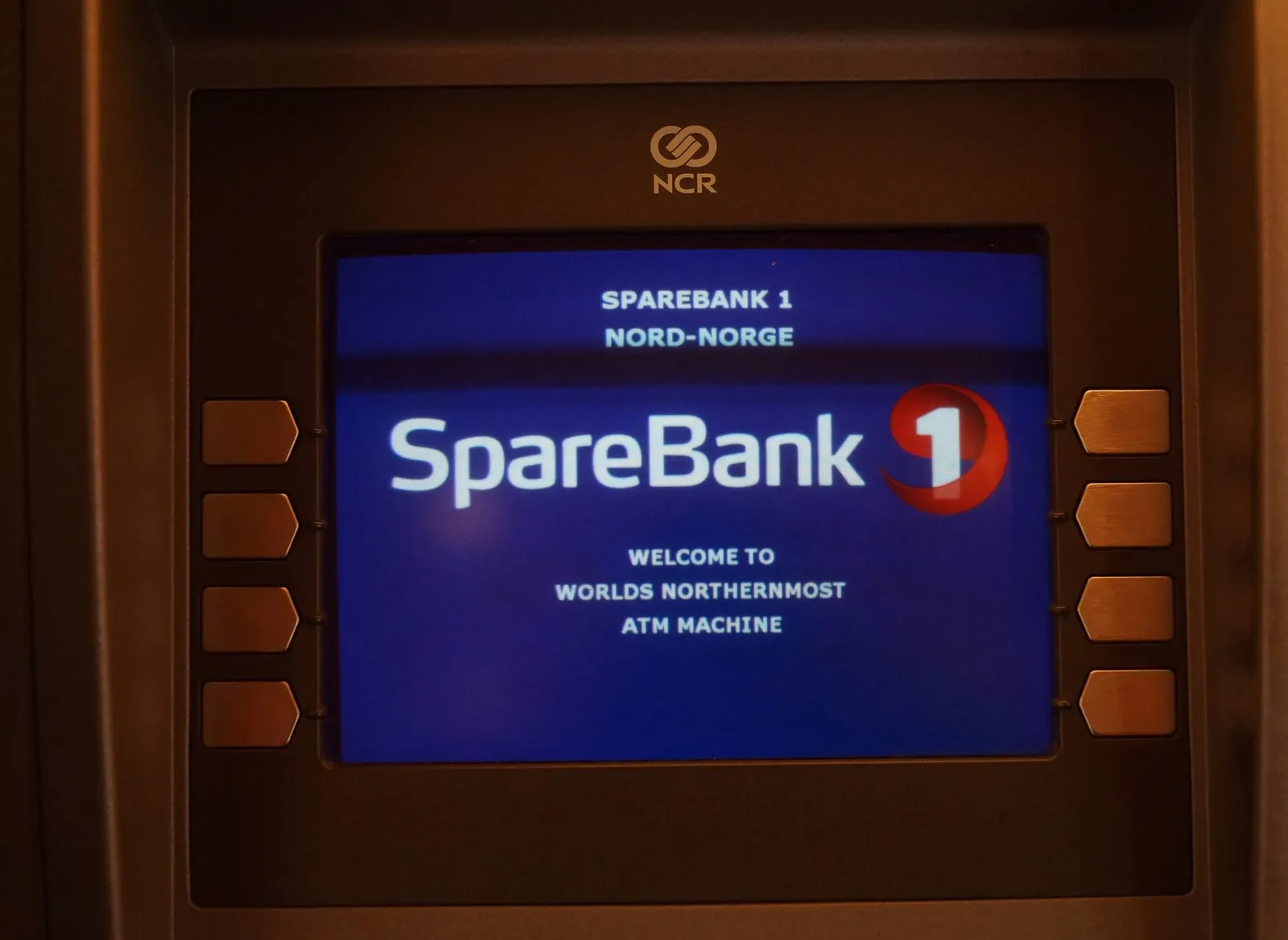 A cash machine screen in a dark frame showing the SpareBank 1 logo and the message Welcome to world's northernmost ATM machine
