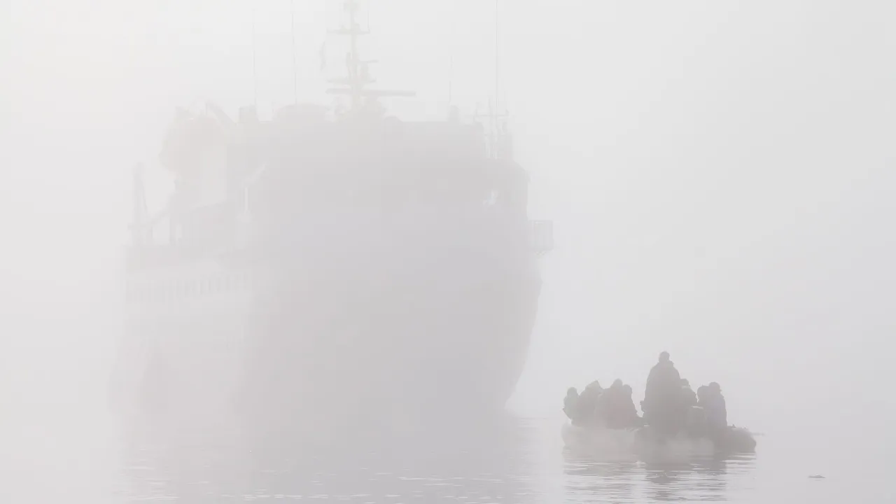 A small inflatable boat with passengers barely visible in thick white fog, with the outline of a ship looming behind